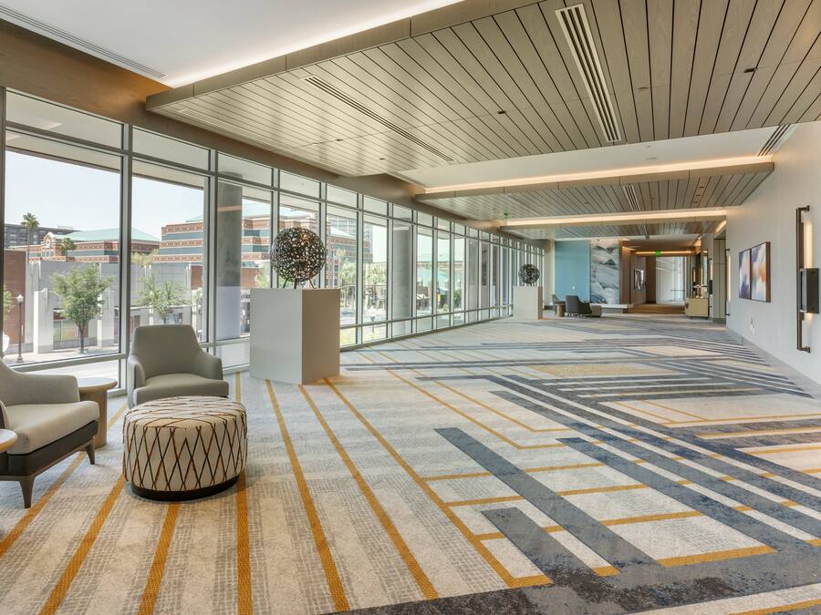 Un vestíbulo amplio con ventanas grandes, alfombra estampada y mobiliario moderno.