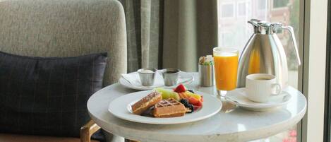 A hotel room with a round table set for breakfast, including waffles, fruit, and a coffee pot.