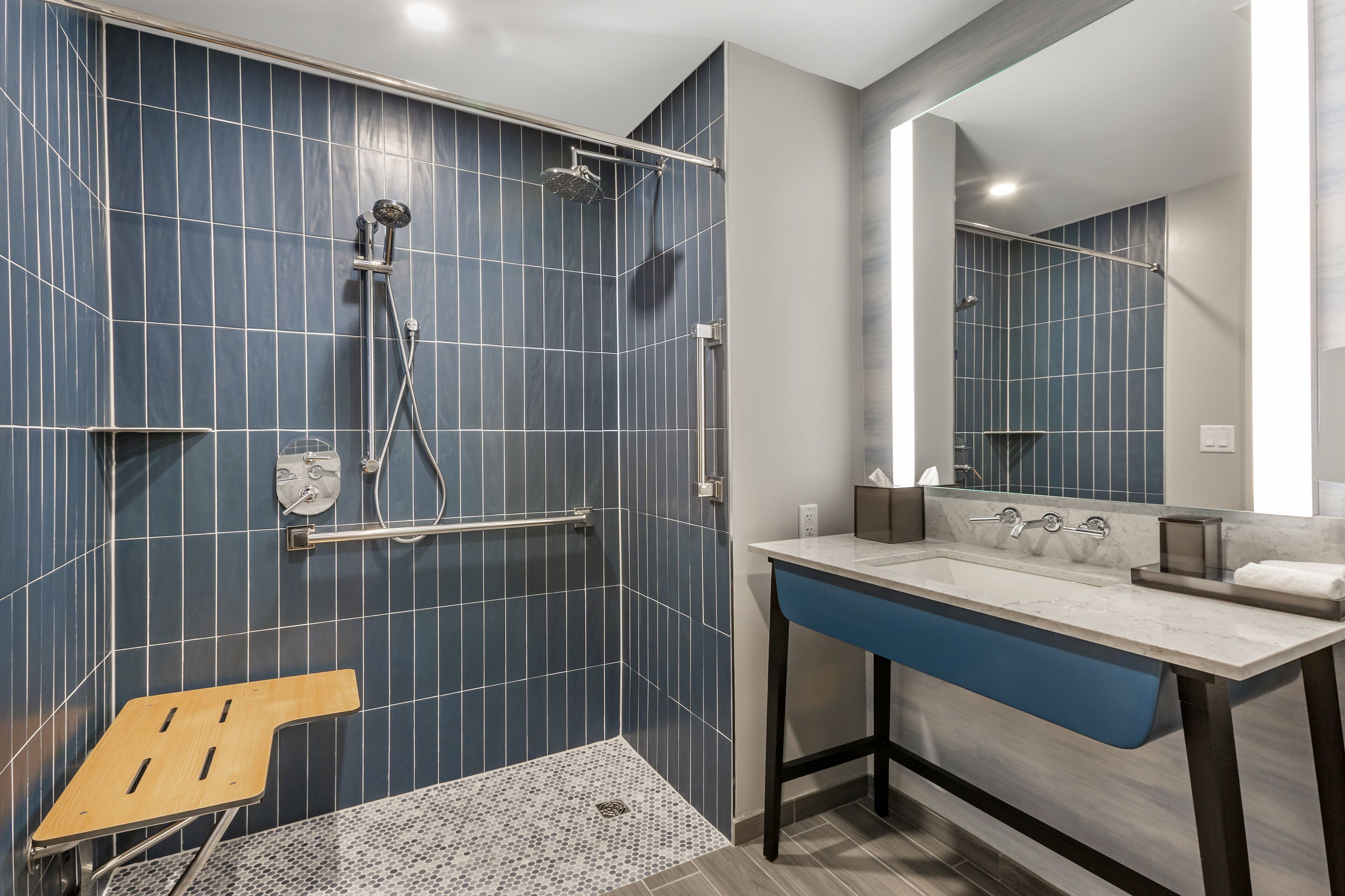 Un baño moderno con ducha, un lavamanos con espejo y un banco de madera.
