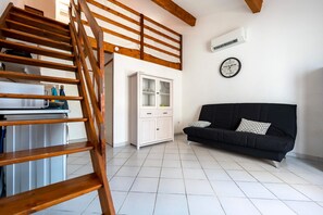 Un escalier menant à une mezzanine où se trouvent un meuble blanc et un canapé noir.