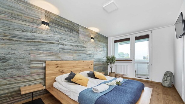 Une chambre moderne avec un lit en bois, un mur en pierre et une vue sur la ville.
