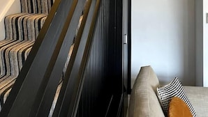 Eine Treppe mit Streifenmuster-Teppich und schwarzen Geländern, ein Blumentopf sowie ein Gemälde an der Wand.