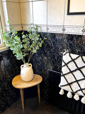 A bathroom with black marble tiles, a white vase with green plants, and a patterned towel on a radiator. - Captivating House in Bangor, Northern Ireland (Bangor)