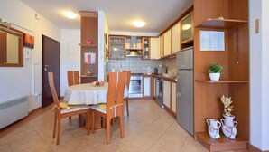A compact kitchen with wooden cabinets, a dining table with chairs, and a small refrigerator.