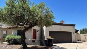 A residential property with a garage, a red door, and a tree in the front yard. - Lakefront Escape | Pool • Spa • 4 Min to Downtown (Chandler)