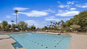 A clear swimming pool with lounge chairs and umbrellas, surrounded by palm trees and a fenced area. - Lakefront Escape | Pool • Spa • 4 Min to Downtown (Chandler)