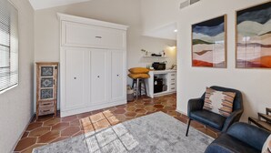 A spacious living area with a large white cabinet, a bar stool, a black leather armchair, and abstract wall art. - Lakefront Escape | Pool • Spa • 4 Min to Downtown (Chandler)