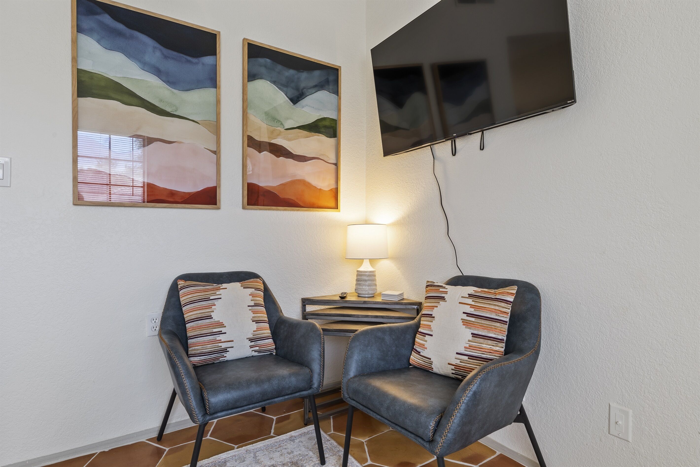 Ett rum med två läderfåtöljer, ett litet bord med en lampa och två abstrakta målningar på väggen.