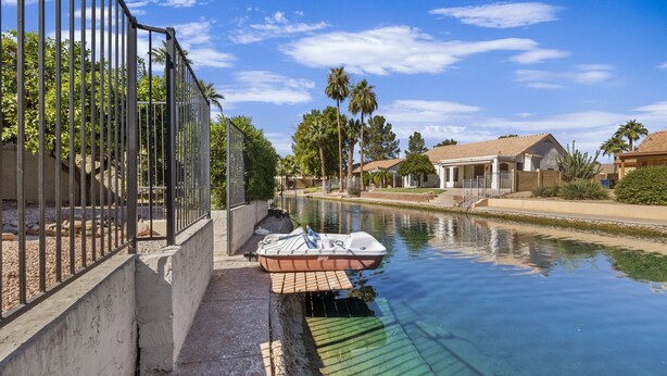 A canal with a boat docked on the right, surrounded by residential houses and palm trees. - Lakefront Escape | Pool • Spa • 4 Min to Downtown (Chandler)