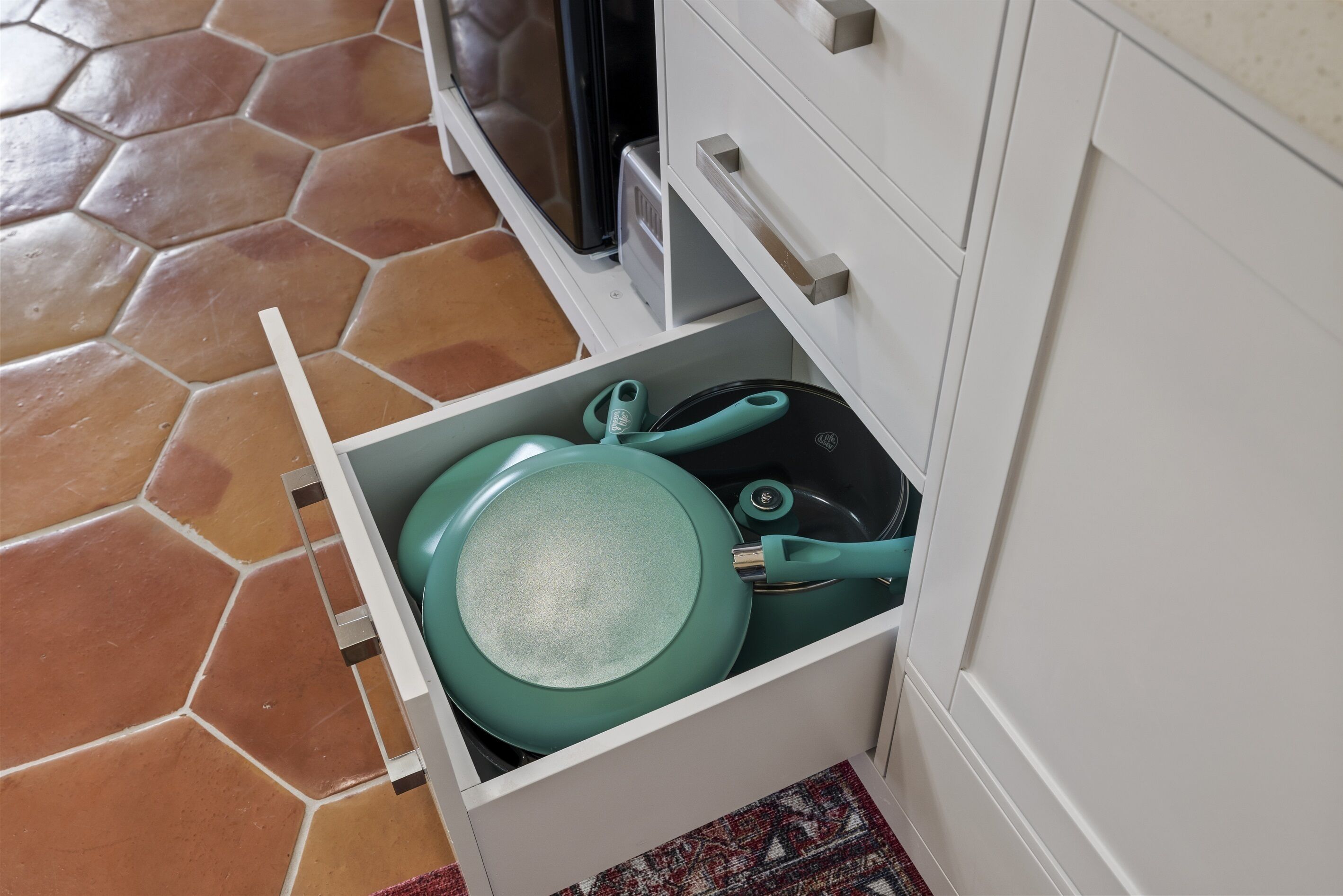 Un cajón de cocina con una sartén verde azulado y una sartén negra.