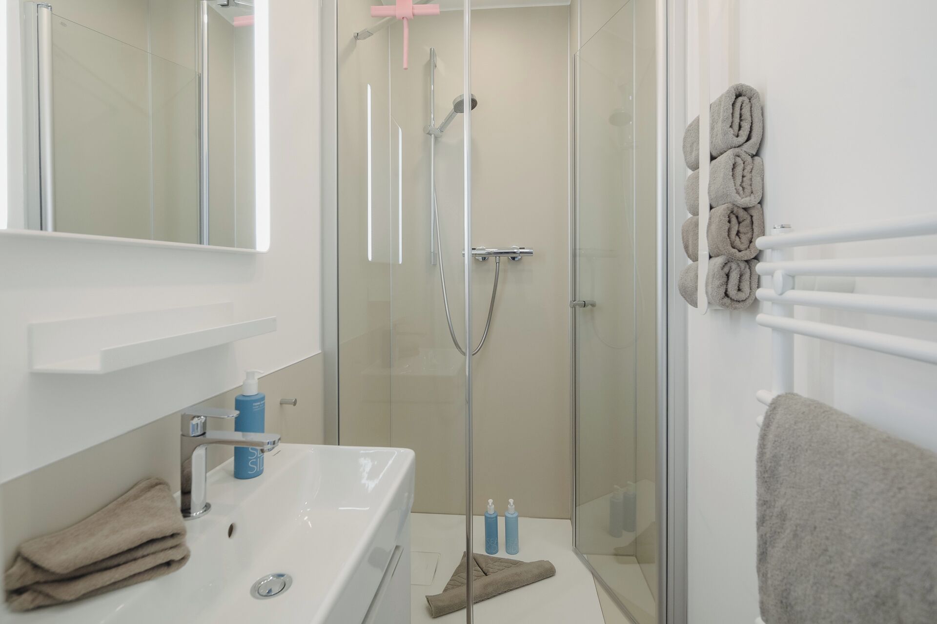 Un bagno con box doccia in vetro, lavandino con specchio e porta asciugamani con asciugamani.