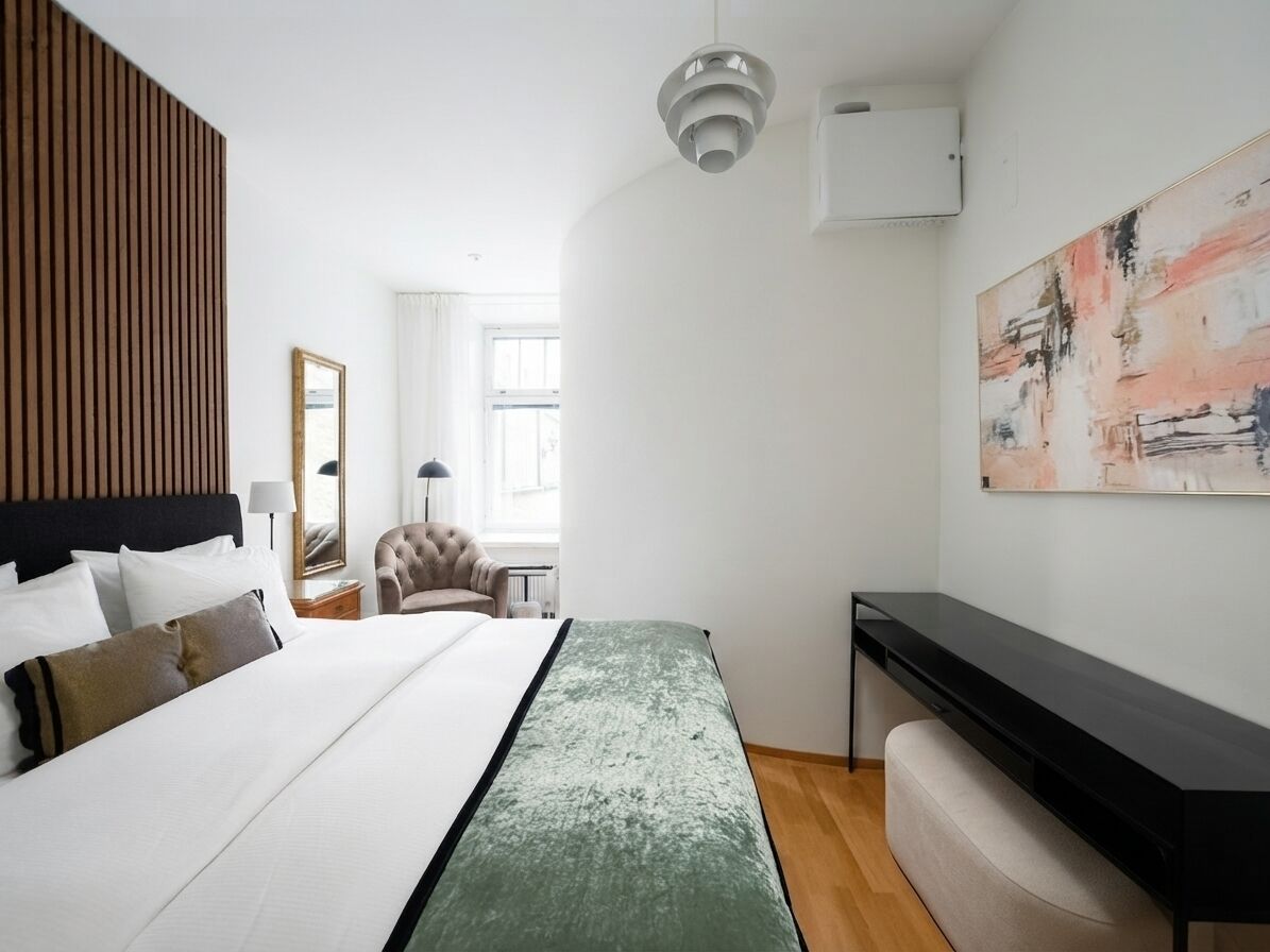 Habitación de hotel con cama, escritorio, silla, ventana y un cuadro en la pared.