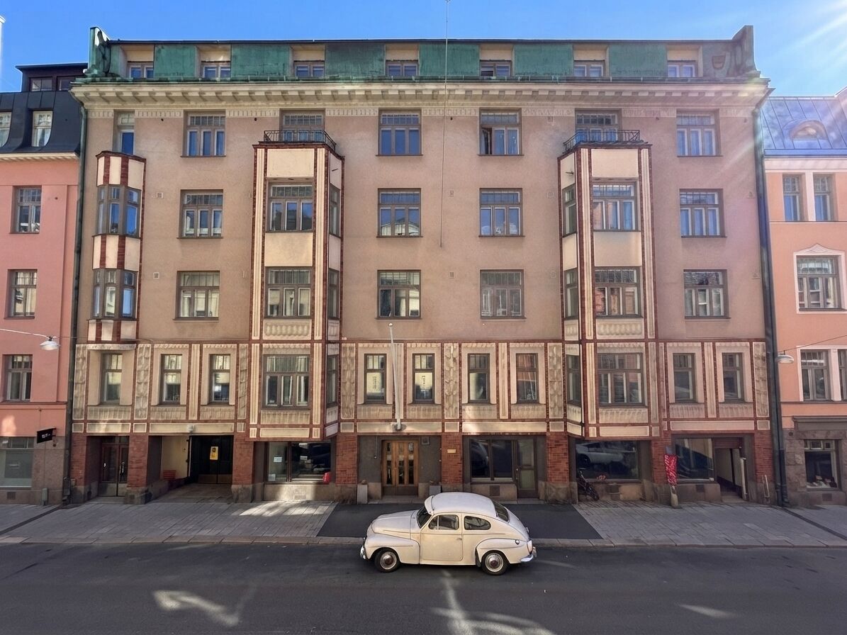Un edificio de varios pisos con una entrada central, un coche estacionado al frente y un cielo despejado.