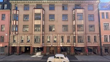 Un edificio de varios pisos con una entrada central, un coche estacionado al frente y un cielo despejado.
