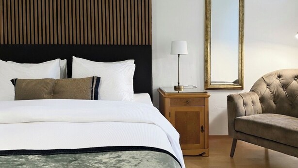 Una habitación de hotel con una cama, una mesita de noche, una lámpara, una silla y un espejo.