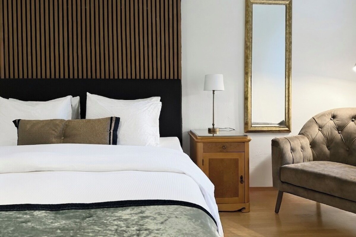 Ein Hotelzimmer mit einem Bett, einem Nachttisch, einer Lampe, einem Sessel und einem Spiegel.