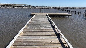 Une jetée en bois s’avançant dans une étendue d’eau calme, avec une plateforme en béton à son extrémité.