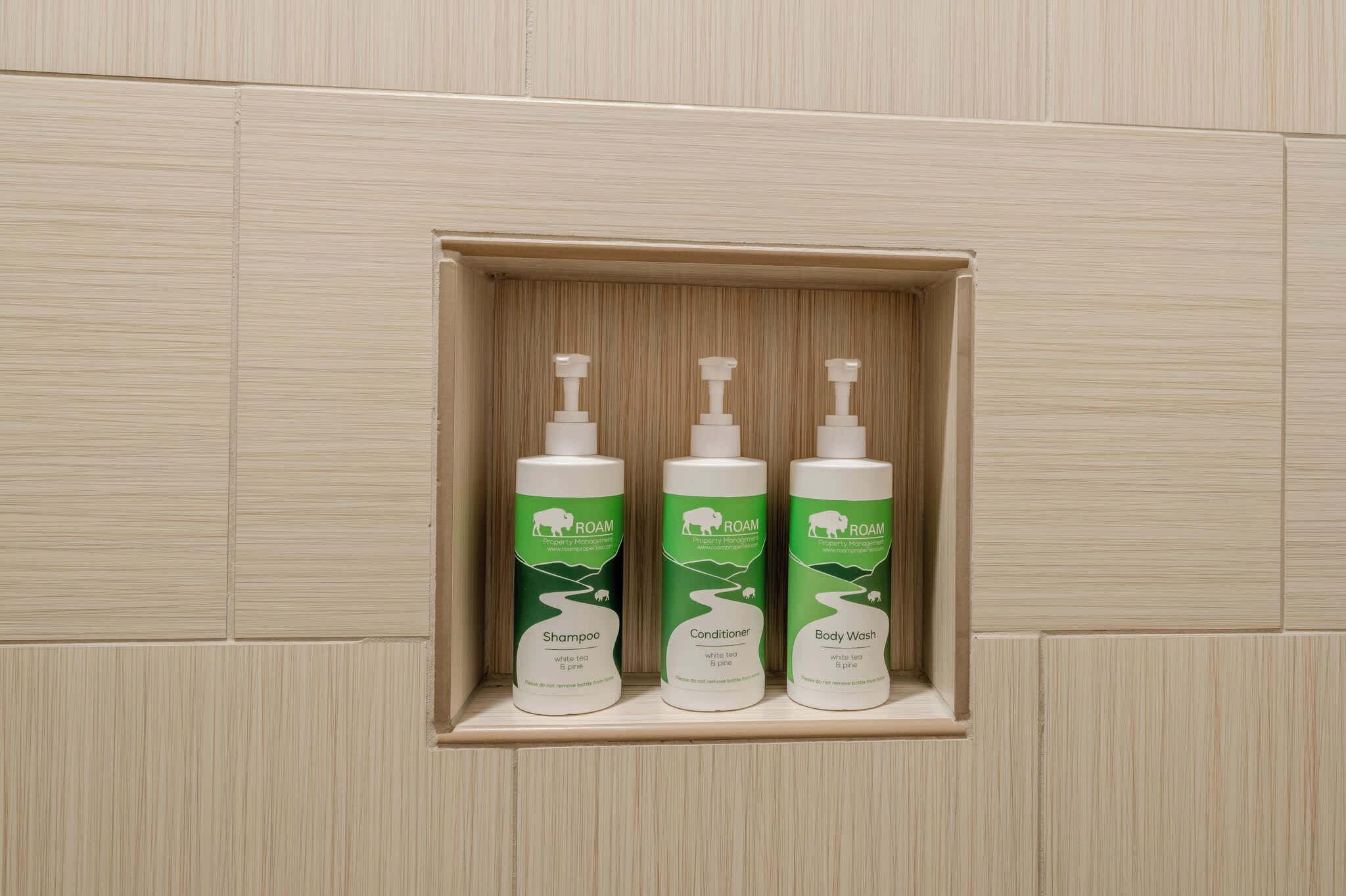 Een badkamerplank met drie flesjes ROAM producten: shampoo, conditioner en douchegel.