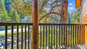 A wooden deck with a metal railing overlooking a rocky stream and dense forest. - One Bedroom plus Loft River View Condo (Alpine Meadows)
