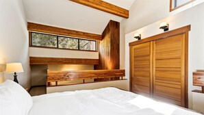 A bedroom with a large bed, wooden headboard, a built-in bench, a wardrobe, and a window with a view of trees. - One Bedroom plus Loft River View Condo (Alpine Meadows)