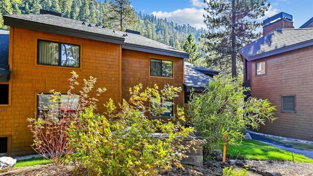 A modern two-story house with a brick facade, large windows, and a well-maintained garden with various shrubs and a small tree. - One Bedroom plus Loft River View Condo (Alpine Meadows)