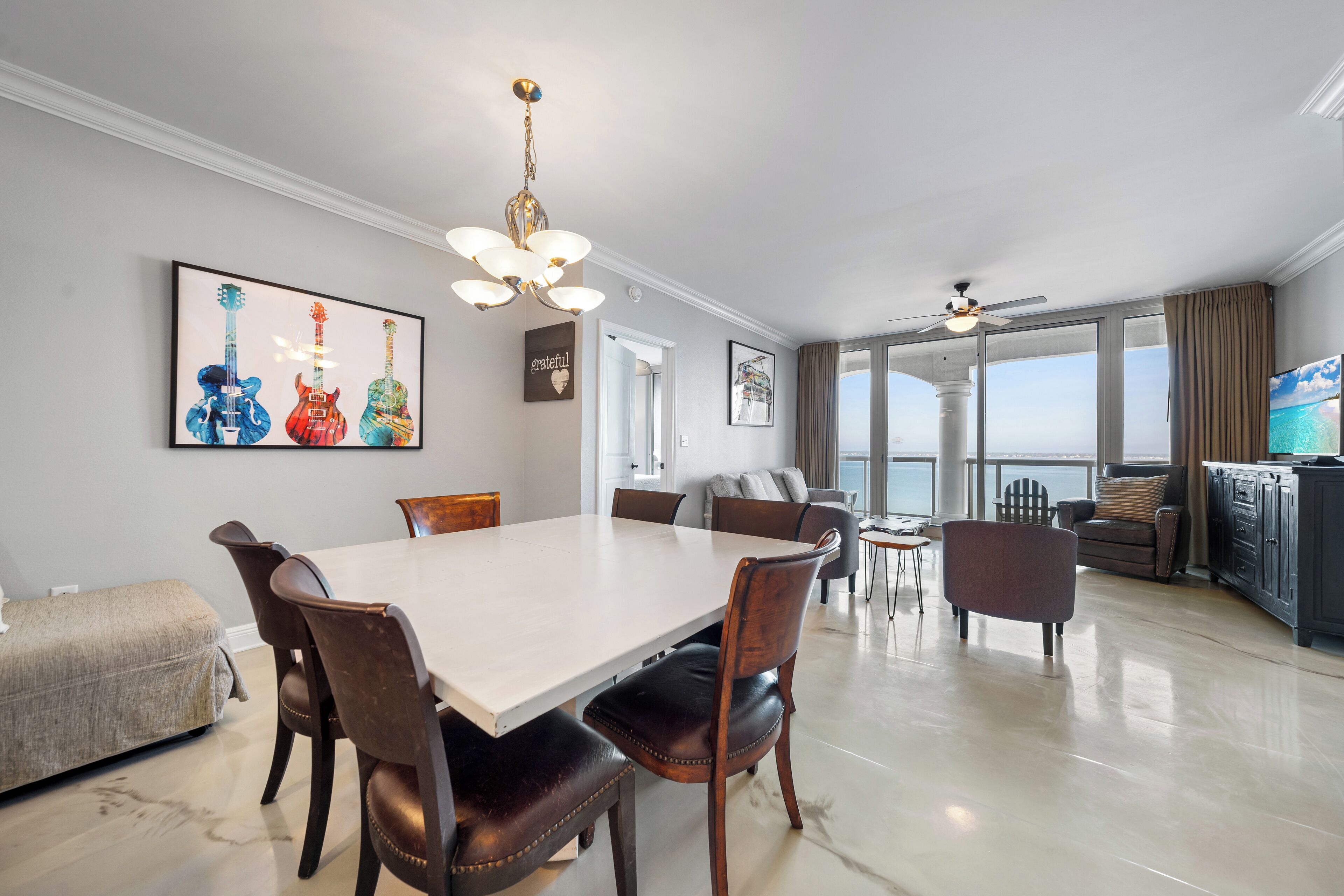 Une salle à manger spacieuse, dotée d’une grande table et de chaises, d’un lustre et offrant une vue sur l’océan grâce à de grandes fenêtres.
