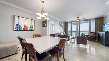 Une salle à manger spacieuse, dotée d’une grande table et de chaises, d’un lustre et offrant une vue sur l’océan grâce à de grandes fenêtres.