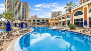 Área de piscina de hotel com espreguiçadeiras e guarda-sóis, cercada por edifícios altos.