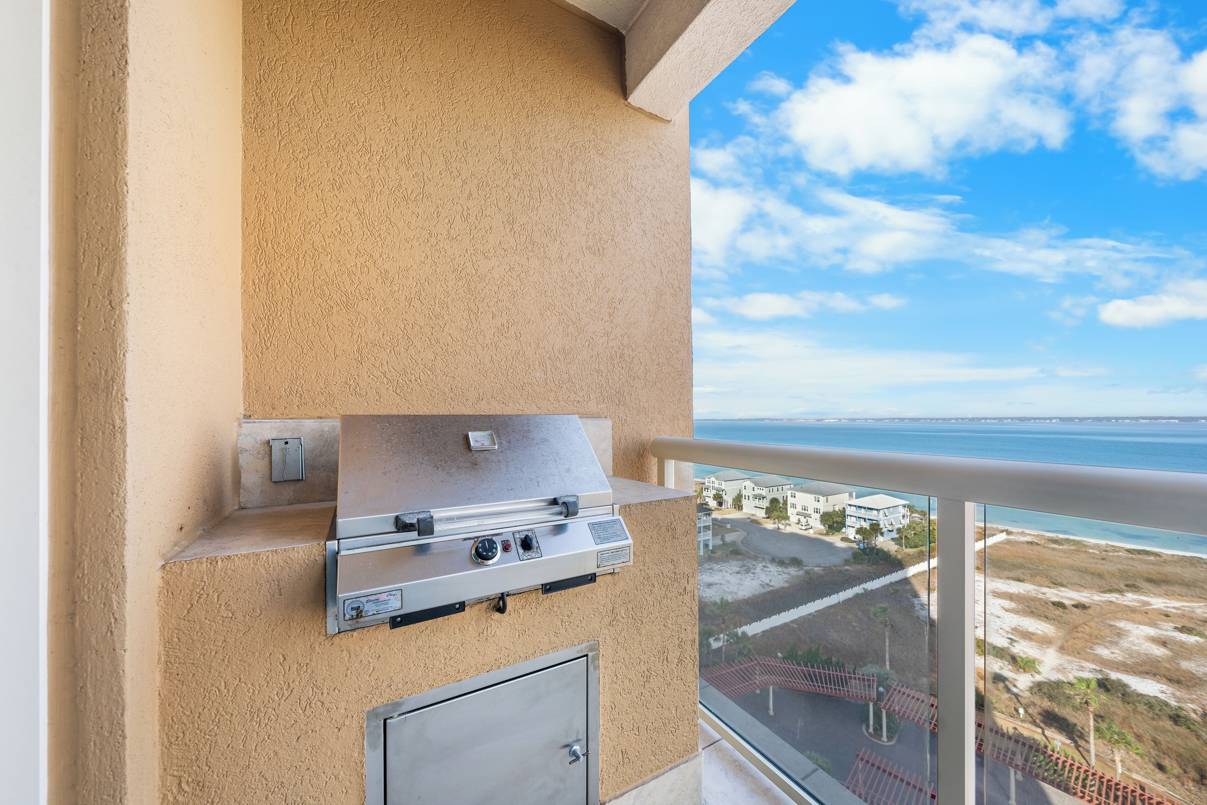 A balcony with a stainless steel grill and a view of the beach and ocean.