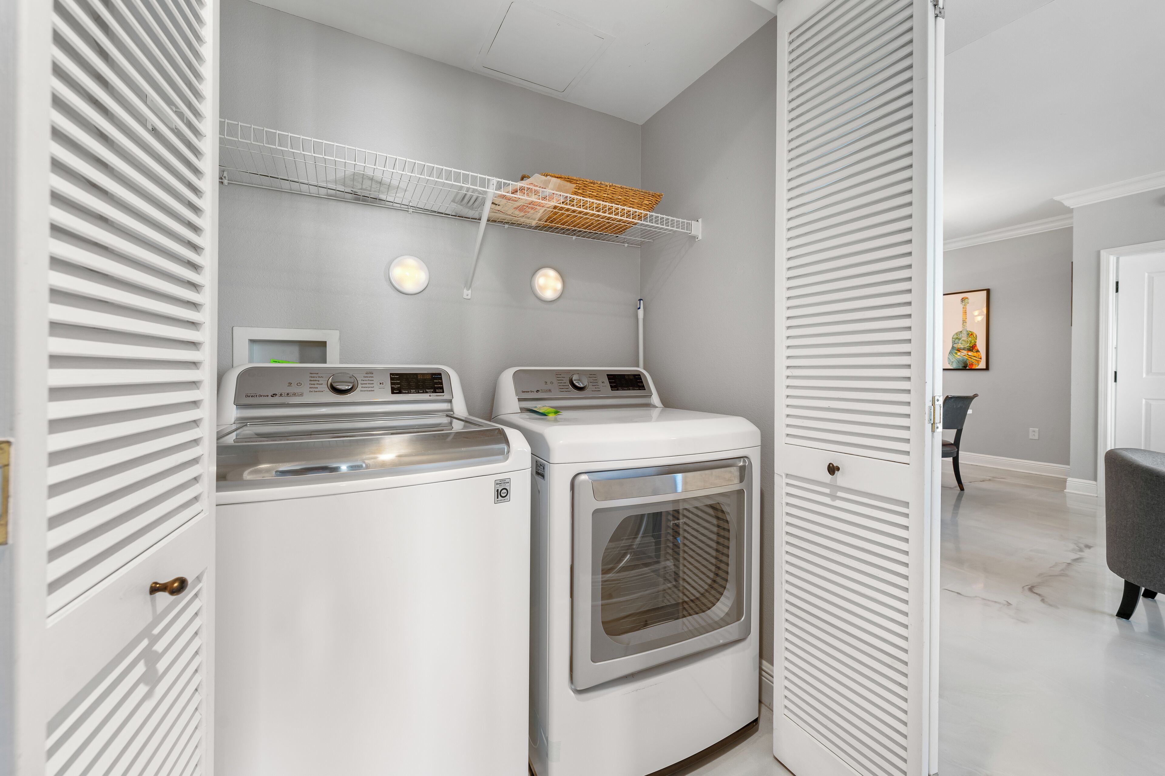 A laundry room with two washing machines and a dryer, a white ceiling, and a door leading to another room.