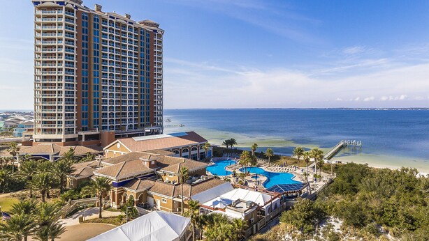Um hotel imponente com uma ampla área de piscina, vista para a praia e um píer que se estende para o oceano.