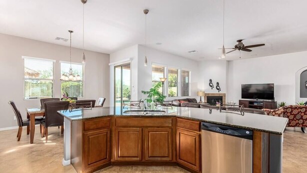 A modern kitchen with a central island, dining area with chairs, and a living room with a sofa and television. - Luxury Stay at Estrella Mountain Ranch (Goodyear)