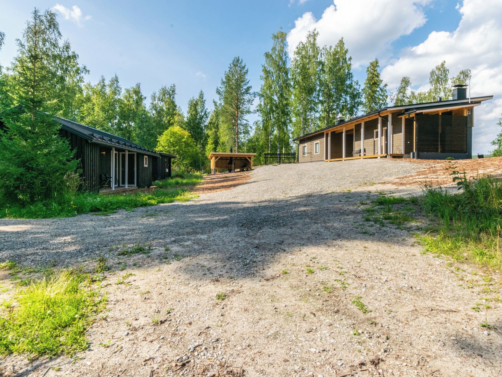 A gravel driveway leading to a building with a covered porch and a small wooden structure.