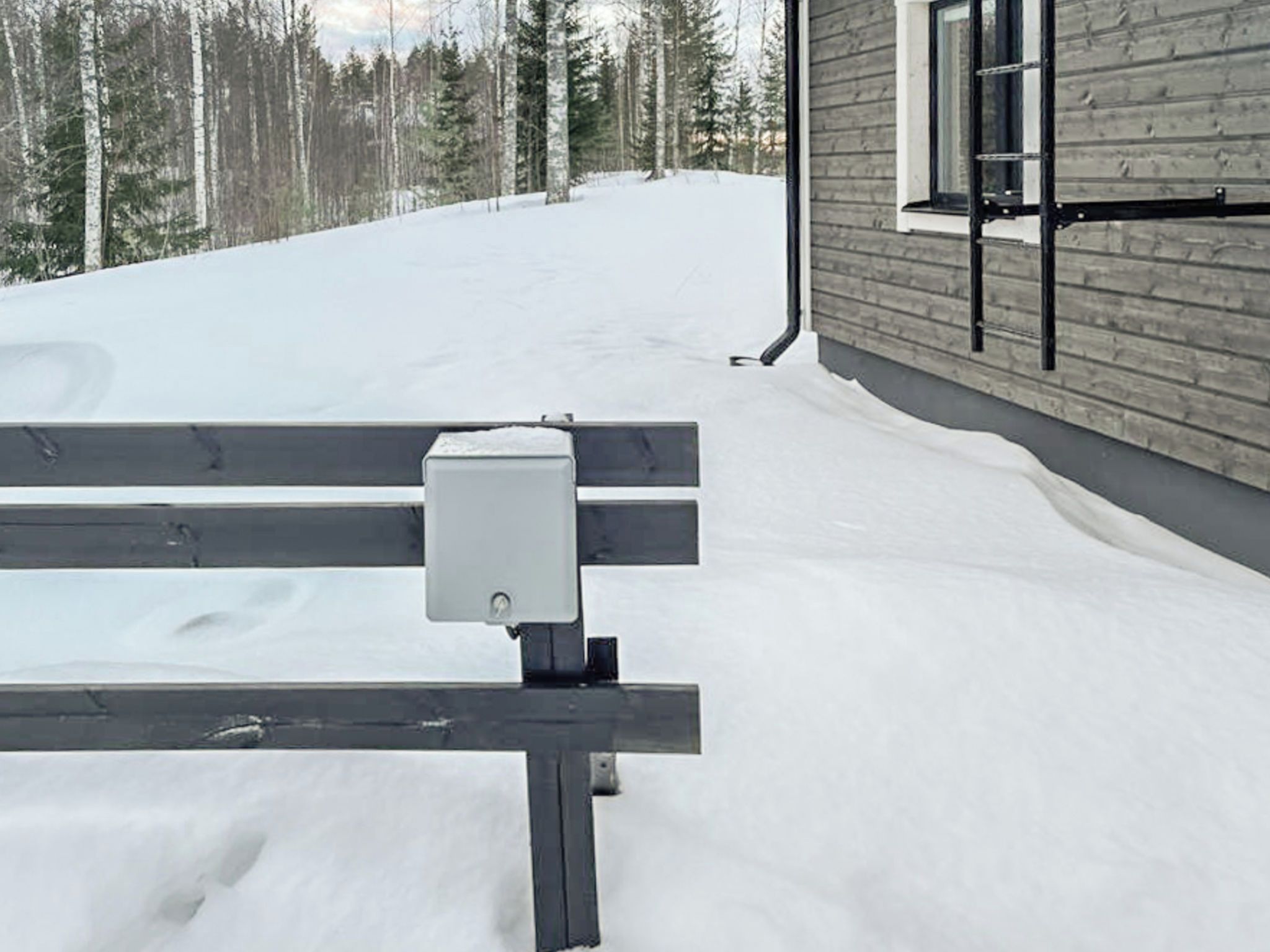 Un banco sobre suelo cubierto de nieve, con un edificio y una ventana al fondo.