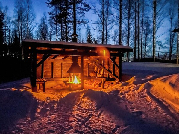 A wooden cabin with a fireplace, surrounded by snow and trees.