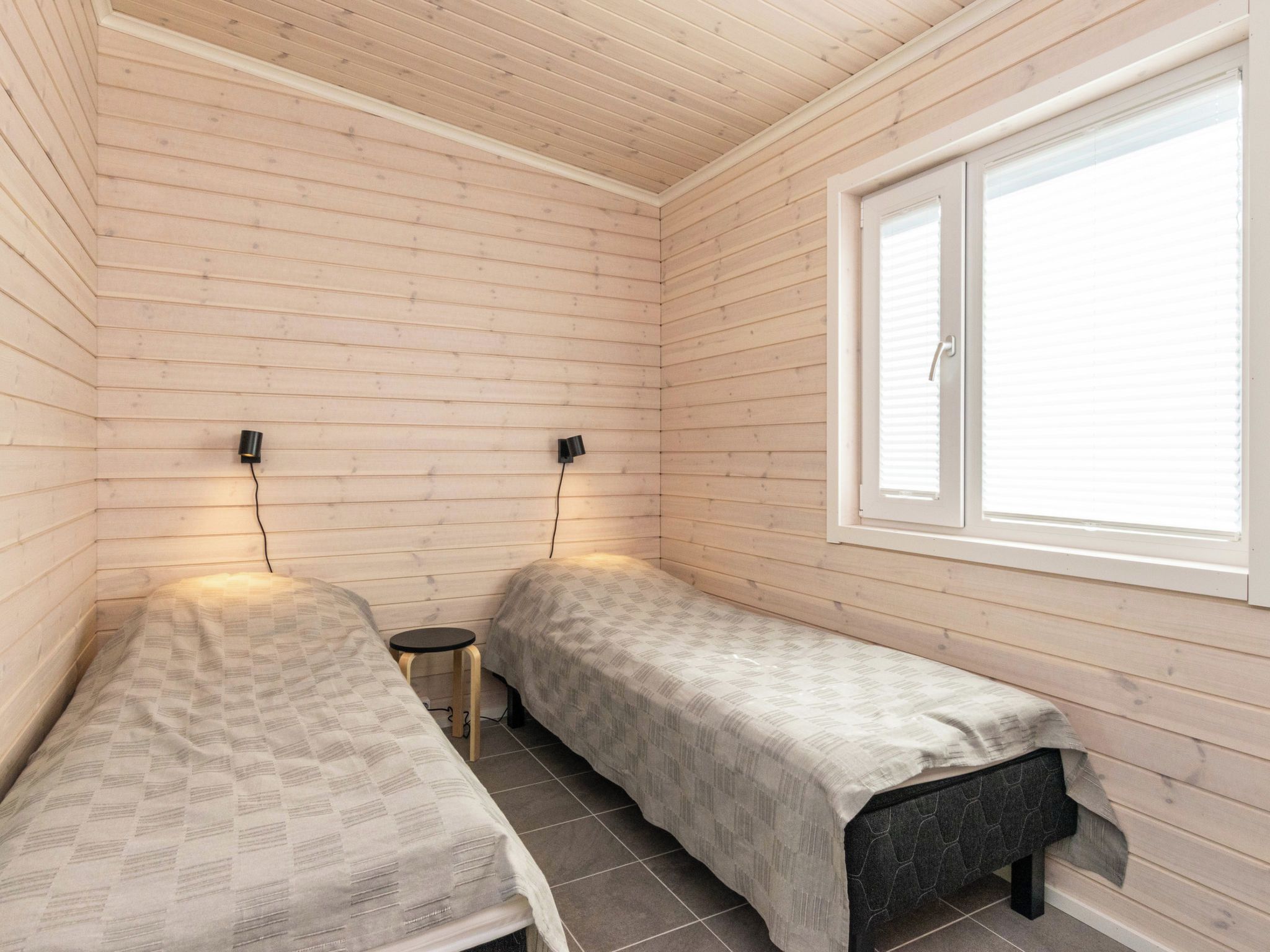 Una habitación pequeña y acogedora con dos camas individuales, una ventana y una lámpara fijada a la pared.