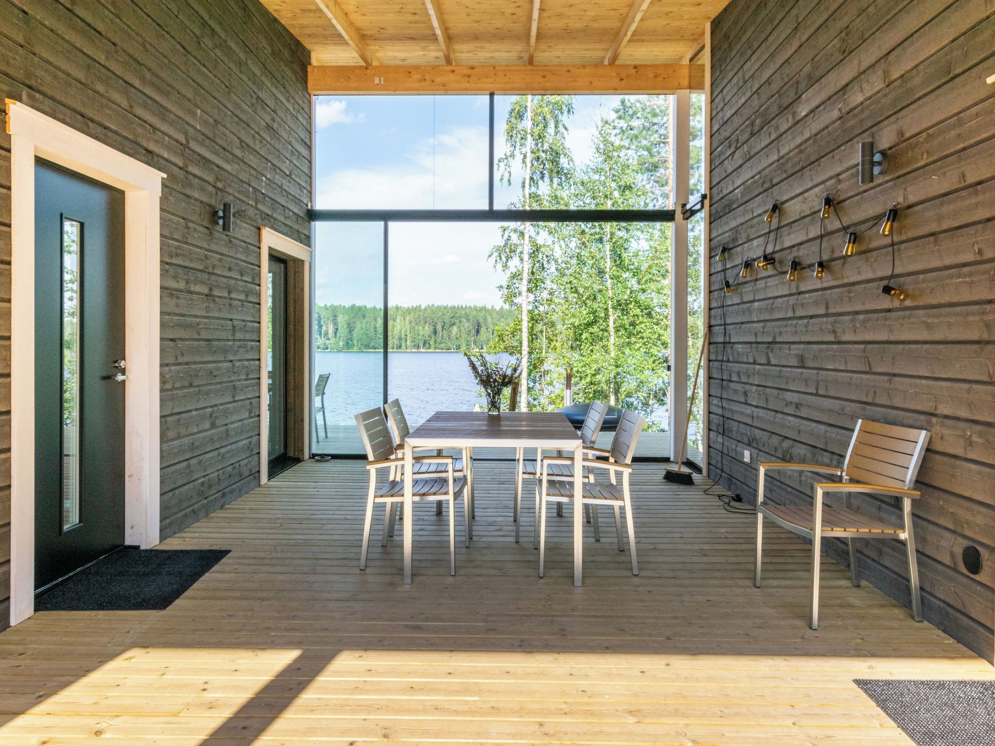 Avokeittiö-oleskelutilalla varustettu hirsihökkelö, jossa on suuri ikkuna, josta avautuu näkymä järvelle ja metsään.