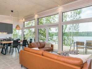 A modern interior with a large window overlooking a lake, a leather sofa, and a dining area.