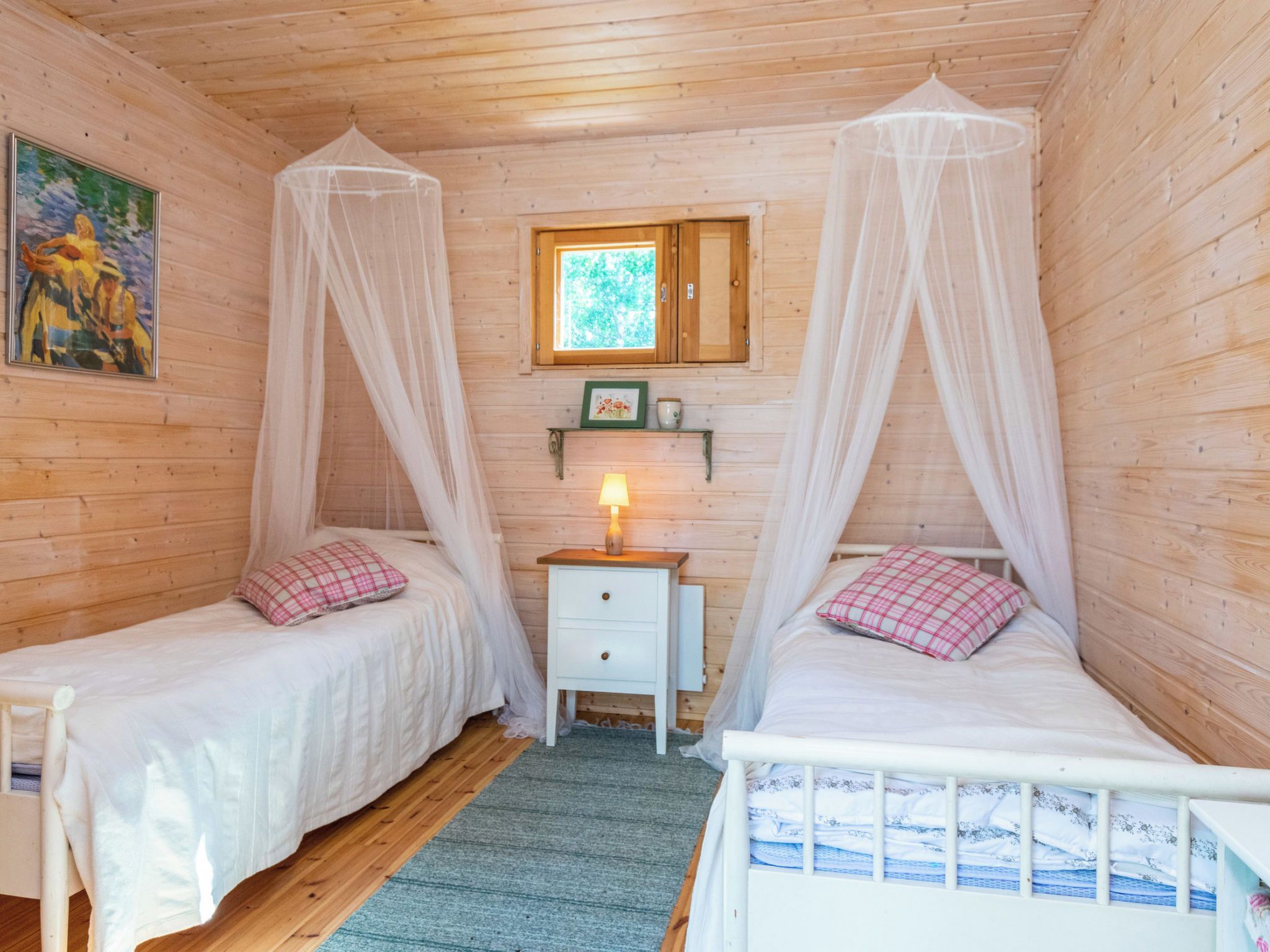 A room with two beds, each with a canopy, a nightstand with a lamp, and a small window with a view of greenery.