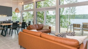 A modern living room with a leather sofa, dining area, and large windows overlooking a lake. - Hot pool cottage kesäranta by Interhome (Enonkoski)