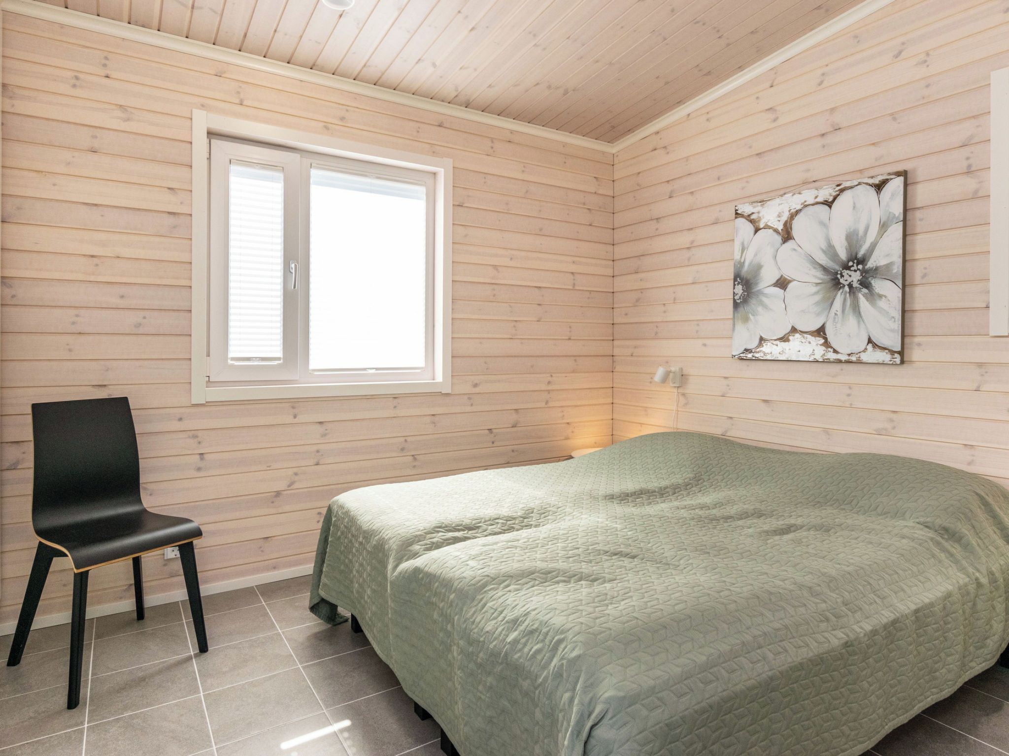 A room with a bed, a chair, a window, and a wall-mounted artwork.