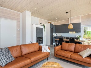 A modern living room with two leather sofas, a fireplace, and a dining area with a kitchen in the background. - Hot pool cottage kesäranta by Interhome (Enonkoski)