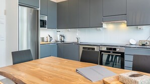 A modern kitchen with grey cabinets, stainless steel appliances, and a wooden dining table. - Hot pool cottage kesäranta by Interhome (Enonkoski)
