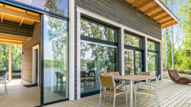 A modern house with a wooden deck, large windows, and a dining area with chairs and a table. - Hot pool cottage kesäranta by Interhome (Enonkoski)