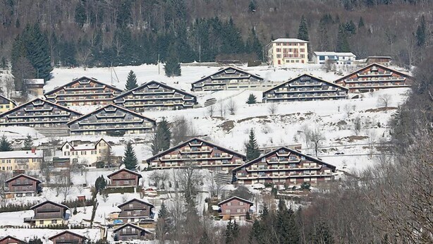 En snötäckt bergsanläggning med stugliknande byggnader, ett centralt hotell och en skog som utgör bakgrunden.