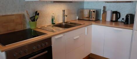 Een moderne keuken met een kookplaat, oven, spoelbak en witte kasten.