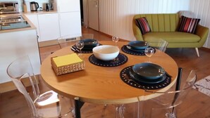 En matplats med ett runt träbord, genomskinliga stolar i glas och en grön soffa i bakgrunden.