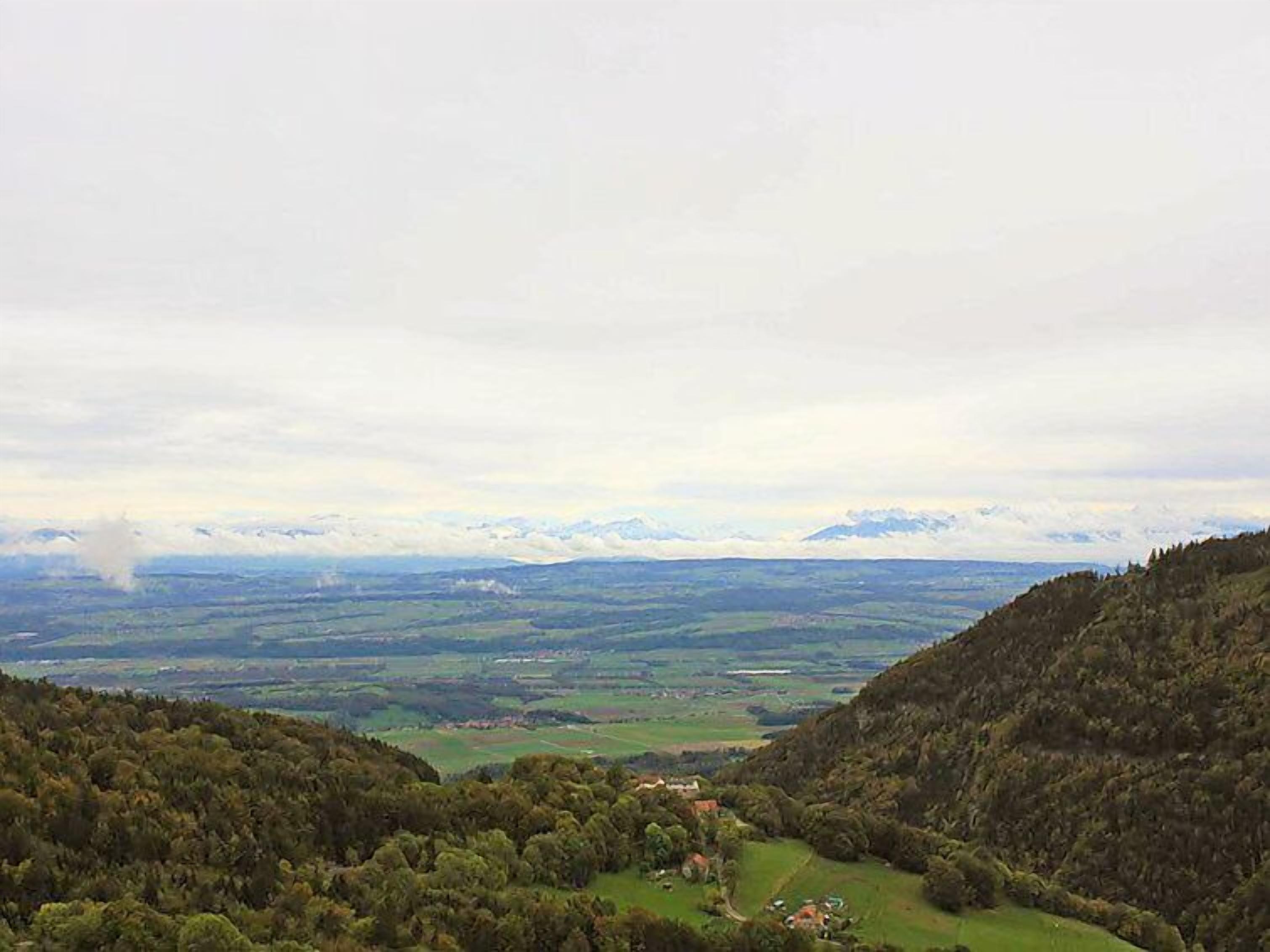 A valley with a small settlement surrounded by forested hills and distant mountains.
