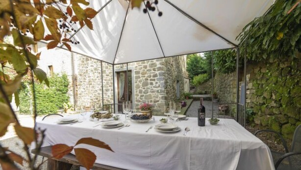Un área de comedor al aire libre con una mesa blanca para cuatro personas, rodeada de muros de piedra y vegetación.