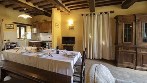 Un comedor con una mesa preparada para cuatro personas, un banco de madera y un televisor sobre un pedestal.